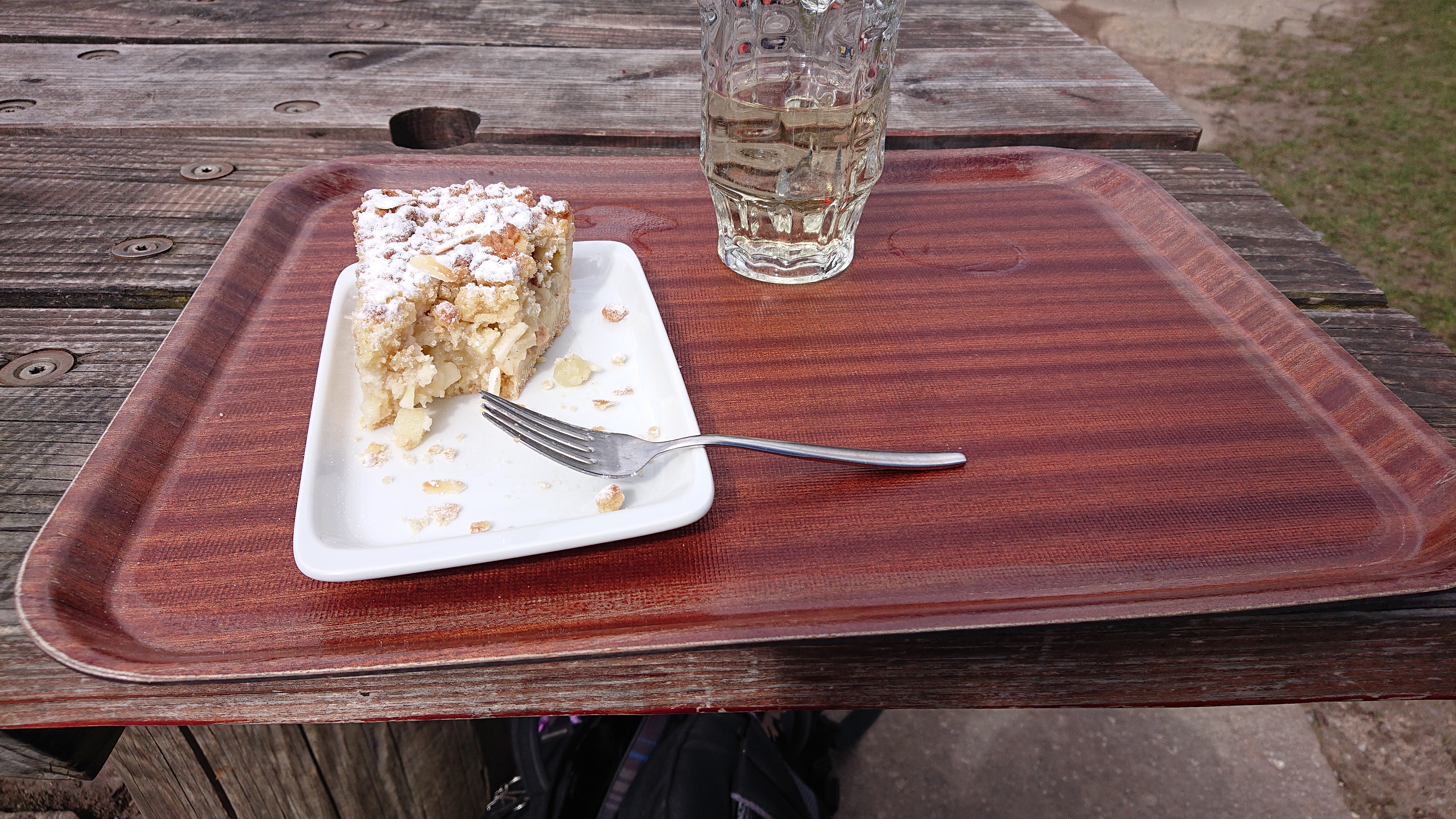Auf dem Bild ist ein Tablet zu sehen. Auf der linken seite ist ein Teller mit teilweise aufgegessenem Apfel-Streuselkuchen und rechts daneben ein Glas mit Apfelschorle